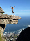 Hiker standing arms raised on the Diving Board rock ledge above Camps Bay, Table Mountain