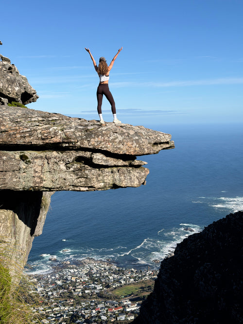 Hiker standing arms raised on the Diving Board rock ledge above Camps Bay, Table Mountain