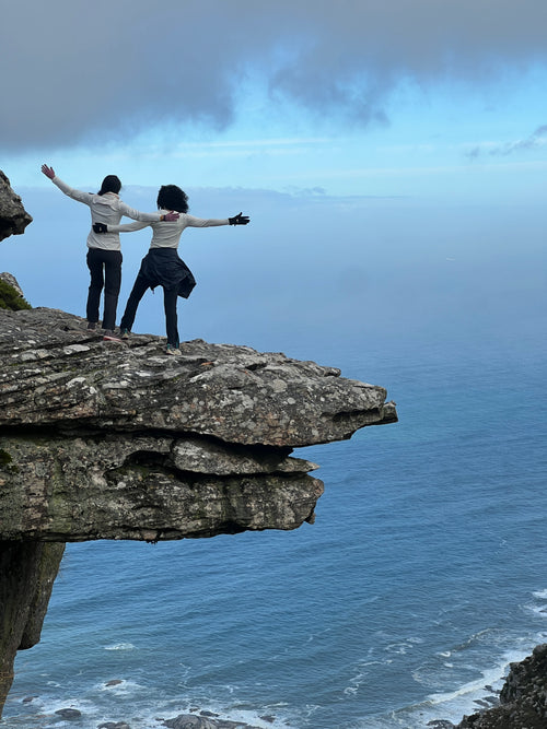 Two hikers with arms outstretched on the Diving Board above a misty Atlantic